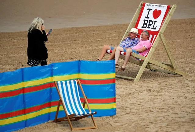 People pose for a photograph in a giant deckchair as rental deckchairs returned to the seafront after a 10 year absence in Blackpool, Britain, June 29, 2021. (Photo by Phil Noble/Reuters)