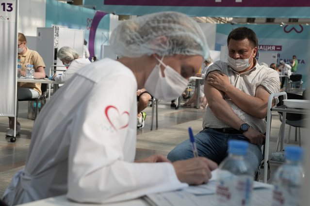 A man holds his arm after receiving a shot of Russia's Sputnik V coronavirus vaccine at a vaccination center in Gostinny Dvor, a huge exhibition place in Moscow, Russia, Monday, July 12, 2021. Russia has been facing a sharp rise of contagions in recent weeks, with daily new infections increasing from around 9,000 in early June to over 25,000 on Friday. (Photo by Pavel Golovkin/AP Photo)