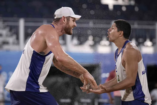Alison Cerutti, left, of Brazil, celebrates with teammate Alvaro Morais Filho after winning a men's beach volleyball match against the Netherlands at the 2020 Summer Olympics, Thursday, July 29, 2021, in Tokyo, Japan. (Photo by Felipe Dana/AP Photo)