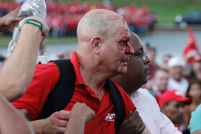 An injured union worker with blood on his face walks towards a line of military police officers to confront them after he was injured by them in a previous encounter, during a protest in Brasilia, Brazil, Tuesday, April 7, 2015. (Photo by Eraldo Peres/AP Photo)