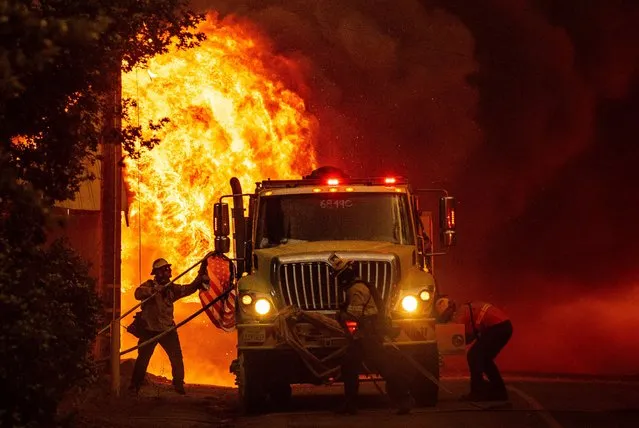 A firefighter saves an American flag as flames consume a home during the Dixie fire in Greenville, California on August 4, 2021. The Dixie fire burned through dozens of homes and businesses in downtown Greenville and continues to forge towards other residential communities. Officials in northern California on August 4, 2021 warned residents of two communities in the path of the raging Dixie fire to evacuate immediately as high winds whipped the flames onwards. (Photo by Josh Edelson/AFP Photo) 