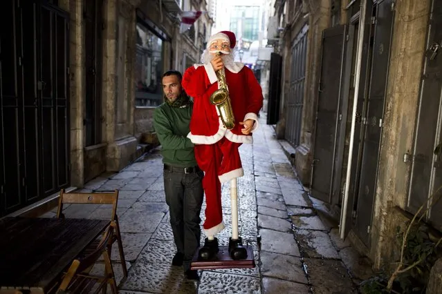 A Palestinian shop owner carries a Santa Claus figure on the street preparing for the Christian holiday of Christmas near Jaffa Gate in the Old City of Jerusalem, Israel, 19 December 2013. (Photo by Abir Sultan/EPA)