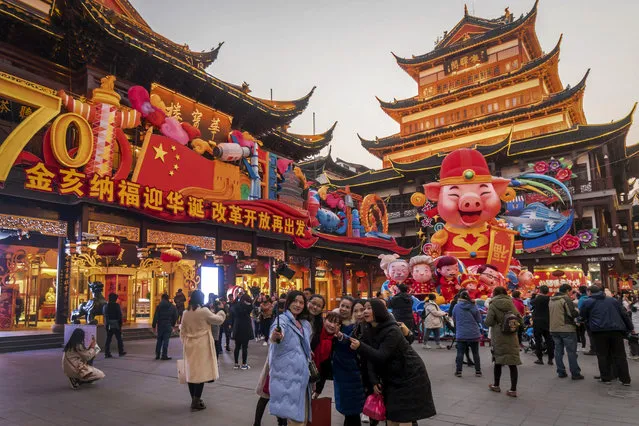In this January 17, 2019, photo, women take a selfie as others tour at the Yu Garden decorated with pig statues for Lunar New Year in Shanghai. China’s 2018 economic growth fell to a three-decade low as activity cooled amid a tariff war with Washington. (Photo by Chinatopix via AP Photo)