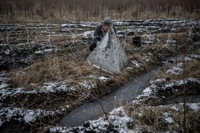 A worker installs razor wire as part of defense structures near a front line in Kharkiv region, Ukraine on December 25, 2023. (Photo by Viacheslav Ratynskyi/Reuters)