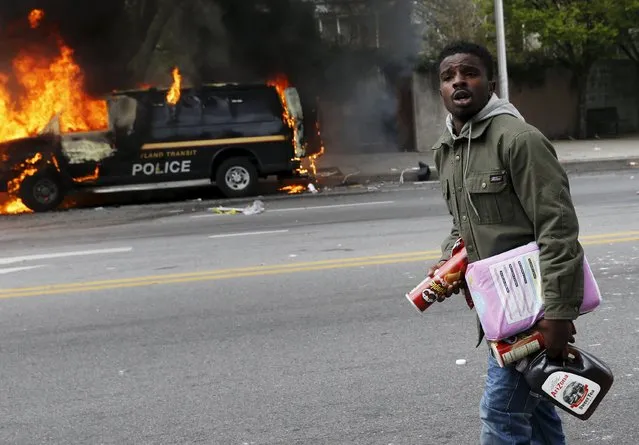 A man with looted goods walks by burned vehicles in Baltimore, Maryland April 27, 2015. (Photo by Shannon Stapleton/Reuters)