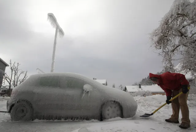 A man shovels ice next to ice-covered car in Postojna February 3, 2014. A quarter of households in Slovenia were left without electricity on Monday after a weekend of blizzards and very low temperatures wreaked havoc on power lines and roads, the national STA news agency reported. (Photo by Srdjan Zivulovic/Reuters)