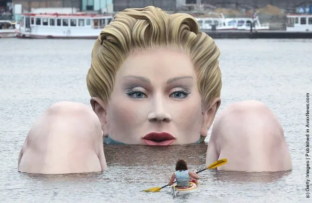 People in boats approach Die Badende (The Bather), a giant sculpture showing a woman's head and knees as if she were resting in the Binnenalster lake in Hamburg, Germany