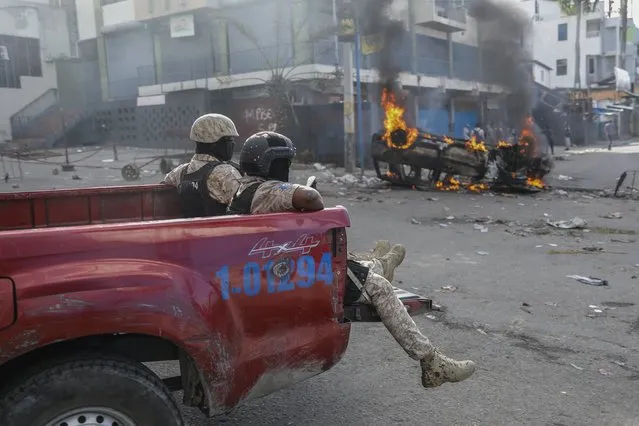 National police officers ride past a vehicle set on fire by protesters during a demonstration demanding the resignation of Prime Minister Ariel Henry, in Port-au-Prince, Haiti, Wednesday, February 7, 2024. (Photo by Odelyn Joseph/AP Photo)