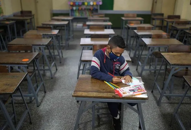 Sebastian, 7, attends math class alone on the first day back to in-person school since the start of COVID-19 pandemic restrictions at the Andres Bello municipal school in Caracas, Venezuela, Monday, October 25, 2021. (Photo by Ariana Cubillos/AP Photo)