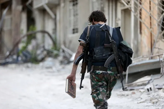 A Free Syrian Army fighter carries a copy of the Koran as he walks along a street in Jobar, a suburb of Damascus, Syria July 6, 2015. (Photo by Bassam Khabieh/Reuters)