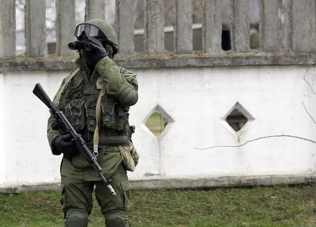 An unidentified armed man stands guard outside a Ukraine infantry base in Privolnoye, Ukraine, Sunday, March 2, 2014. Hundreds of unidentified gunmen arrived outside Ukraine's infantry base in Privolnoye in its Crimea region. The convoy includes at least 13 troop vehicles each containing 30 soldiers and four armored vehicles with mounted machine guns. The vehicles – which have Russian license plates – have surrounded the base and are blocking Ukrainian soldiers from entering or leaving it. (Photo by Darko Vojinovic/AP Photo)