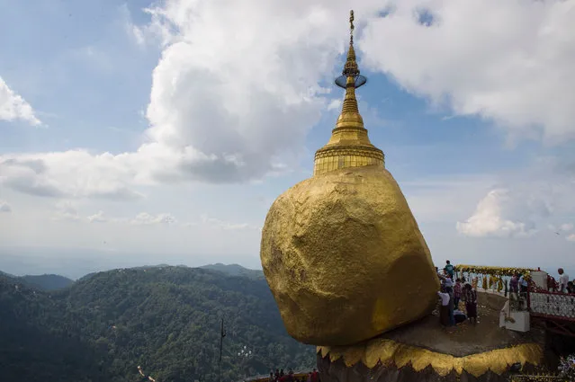 In this photograph taken on December 25, 2016, devotees pray before a huge rock especially covered with layers of gold at Kyaiktiyo pagoda on Mt. Kyaiktiyo A popular Buddhist pilgrimage site and a tourist attraction in Myanmar' s Mon State, the Kyaiktiyo pagoda, also known as Golden Rock, rests by the the edge of a granite boulder covered with gold leaves pasted on by devotees. According to legend, the Golden Rock is perched on a strand of Buddha' s hair while others admire it as a natural rock formation. (Photo by Romeo Gacad/AFP Photo)