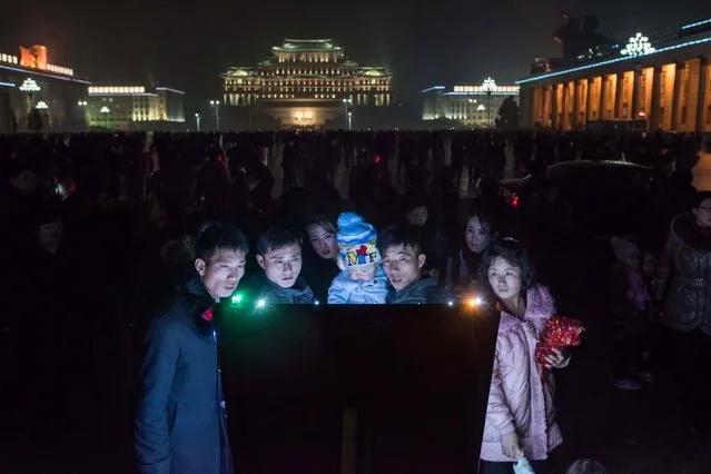 People look at a noticeboard after a fireworks display in front of Kim Il-Sung square as they visit an ice festival near the Taedong river, on the occasion of the 75th anniversary of the birth of Kim Jong-Il, in central Pyongyang on February 16, 2017. North Korean newlyweds, soldiers and children lined up to laud their country's rulers on February 16, the birthday of the late Kim Jong-Il, father of both the current leader and the exiled renegade assassinated in Malaysia this week. (Photo by Ed Jones/AFP Photo)