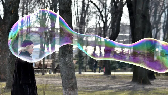 A woman walks next to a soap bubble made by a street artist in the center of Ukrainian capital of Kiev on a sunny day on March 15, 2017. (Photo by Sergei Supinsky/AFP Photo)