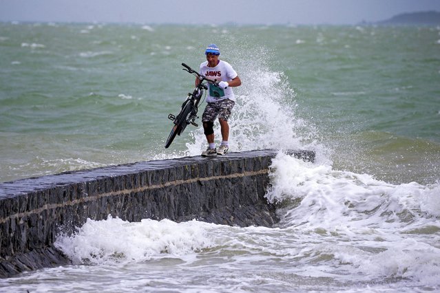 A man stands on breakwater with his bike along the waterfront in Auckland, New Zealand, Sunday, February 12, 2023. New Zealand's national carrier has canceled dozens of flights as Aucklanders brace for a deluge from Cyclone Gabrielle, two weeks after a record-breaking storm swamped the nation's largest city and killed several people. (Photo by Alex Burton/NZ Herald via AP Photo)