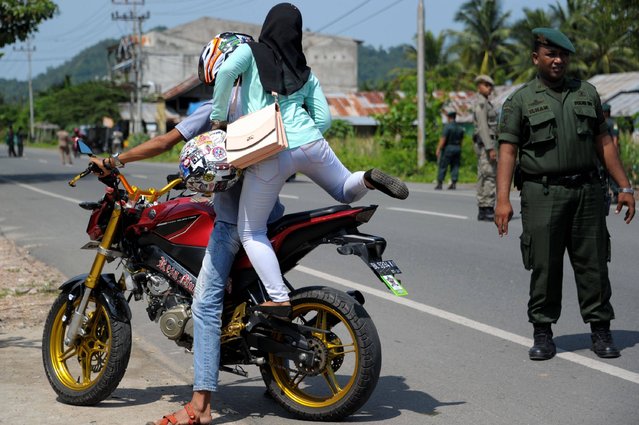 An Indonesian Aceh province sharia policeman (R) stops motorists for wearing jeans and the manner the woman (C) is sitting on the motorbike in Aceh Besar, Aceh province, on May 10, 2016. The province on northern Sumatra island has banned Muslim women from wearing figure-hugging clothing such as tight trousers and women passengers must sit side-saddle on motorbikes under Islamic by-laws that have outraged less conservative parts of the mainly Muslim archipelago. Aceh is the only province in the predominantly Muslim country that applies sharia law, and public canings for breaches of Islamic code happen on a regular basis and often attract huge crowds. (Photo by Chaideer Mahyuddin/AFP Photo)