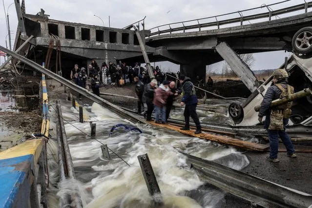 Local residents cross a destroyed bridge as they evacuate from the town of Irpin, after days of heavy shelling on the only escape route used by locals, while Russian troops advance towards the capital, near Kyiv, Ukraine on March 7, 2022. (Photo by Carlos Barria/Reuters)