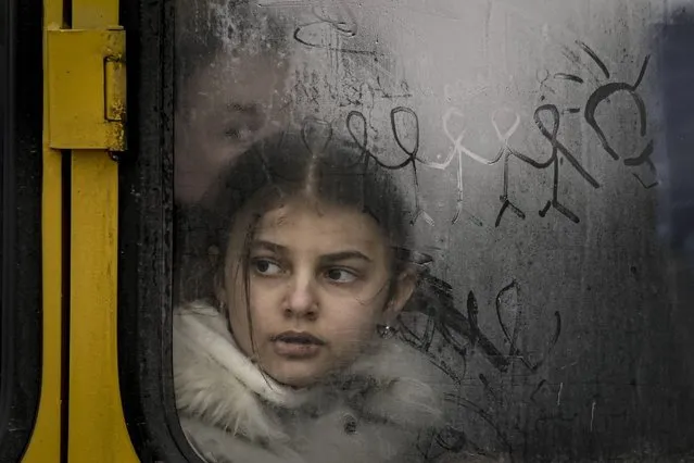 A child looks out a steamy bus window with drawings on it as civilians are evacuated from Irpin, on the outskirts of Kyiv, Ukraine, Wednesday, March 9, 2022. A Russian airstrike devastated a maternity hospital Wednesday in the besieged port city of Mariupol amid growing warnings from the West that Moscow's invasion is about to take a more brutal and indiscriminate turn. (Photo by Vadim Ghirda/AP Photo)