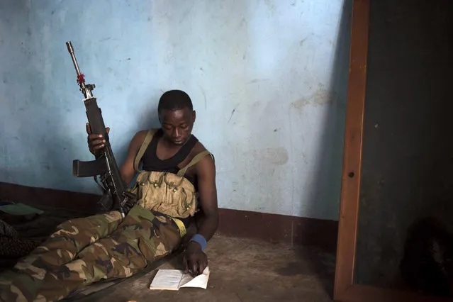 A Seleka fighter reads a book while holding a gun on a base, where 500 Seleka fighters are confined, in Bangui, Central African Republic, February 25, 2014. According to the men, they dare not leave the base, where they agreed to confine themselves with the French and African peacekeeping missions, for fear of being killed by anti-balaka militiamen. (Photo by Camille Lepage/Reuters)