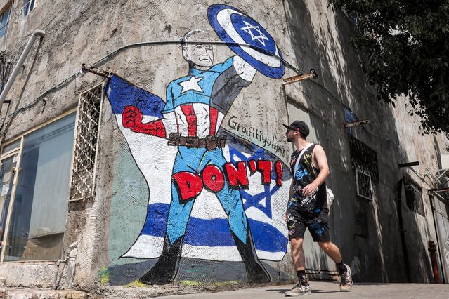 A man walks past a mural drawn by the “Grafitiyul” graffiti art group depicting US President Joe Biden dressed as the Marvel comics character “Captain America” standing before an Israeli flag and holding up his shield depicting the Star of David symbol, along a street in Tel Aviv on April 15, 2024. Iran launched more than 300 drones and missiles towards Israel late on April 13 in an unprecedented overnight attack injuring at least 12 people. Israel's army on April 14 said Israel, the United States, Britain, France and other allies had come together as a “coalition” for the first time to counter Iran's unprecedented attack. (Photo by Jack Guez/AFP Photo)