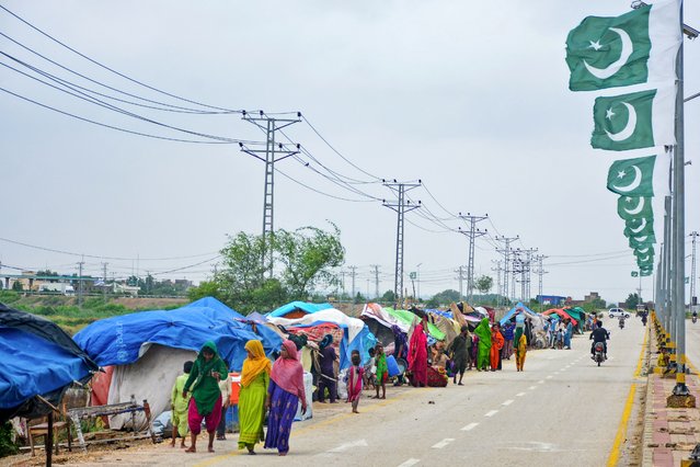 Flood-affected people walk past their make-shift tents along a roadside after heavy monsoon rains in Hyderabad, Sindh province on August 30, 2024. Twelve people died on August 30, when a landslide triggered by heavy rains destroyed their house in Pakistan, rescue officials said, with more than 300 killed since the start of monsoon season. (Photo by Akram Shahid/AFP Photo)