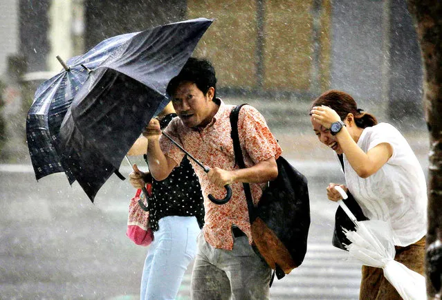 People holding umbrellas walk against strong winds and heavy rain brought about by Typhoon Neoguri on a street in Naha, on Japan's southern island of Okinawa, in this photo taken by Kyodo July 9, 2014. Torrential rains battered Japan's Okinawa islands on Wednesday as a weakened but still dangerous typhoon, leaving two dead and threatening widespread flooding as it headed for the nation's main islands. (Photo by Reuters/Kyodo)
