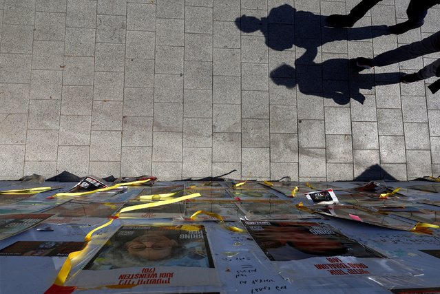 People's shadows are cast as they walk near posters with images of hostages kidnapped in the deadly October 7 attack on Israel by the Palestinian Islamist group Hamas, in Tel Aviv, Israel on April 16, 2024. (Photo by Hannah McKay/Reuters)