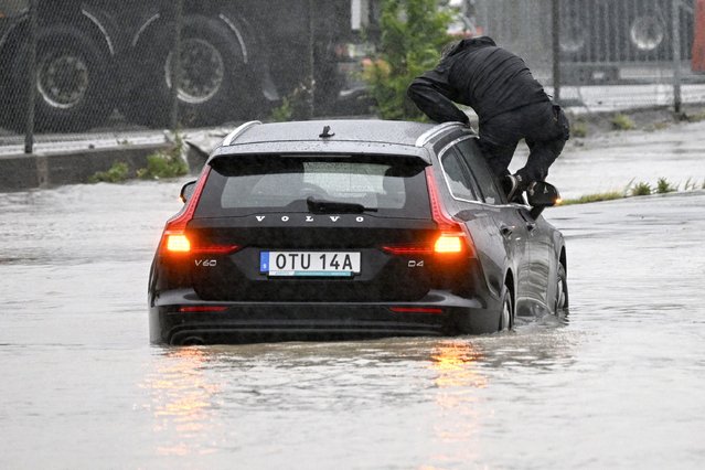 A man climbs out of a car which got stuck at a flooded roundabout in Arlöv, along the E6 road outside Malmö, southern Sweden, Monday, August 7, 2023. Stormy weather across the Baltic Sea region is causing airport delays, suspended ferry service, minor power outages and lots of rain. (Photo by Johan Nilsson/TT News Agency via AP Photo)