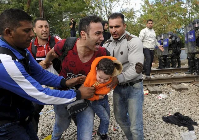 A migrant reacts as he carries a child during clashes with Macedonian police at the Greek-Macedonian border, August 21, 2015. (Photo by Alexandros Avramidis/Reuters)