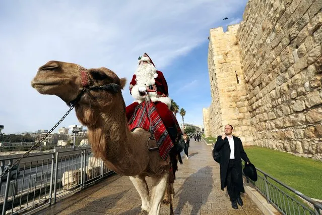 Dressed as Santa Claus, Issa Kassissieh sits astride a camel as he visits Jaffa Gate in Jerusalem's Old City, December 23, 2021. (Photo by Ammar Awad/Reuters)