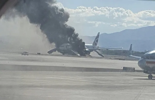 In this photo taken from the view of a plane window, smoke billows out from a plane that caught fire at McCarren International Airport, Tuesday, September 8, 2015, in Las Vegas. An engine on the British Airways plane caught fire before takeoff, forcing passengers to escape on emergency slides. (Photo by Eric Hays via AP Photo)