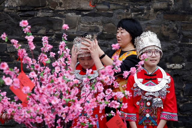A teacher adjusts the crown of Hill Street student Ayla Zheng 9, as Luo Yi Ye 10, looks on while standing next to a cherry blossom wishing tree dressed in the traditional clothing of the Miao ethnic group of China to welcome the Lunar New Year community celebration of the year of the snake, in Dublin, Ireland on January 20, 2025. (Photo by Clodagh Kilcoyne/Reuters)