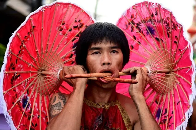 A devotee of the Kuan Tae Kun shrine with paper umbrellas pierced through his cheeks takes part in a procession during the annual Vegetarian Festival in Phuket on September 28, 2022. (Photo by Manan Vatsyayana/AFP Photo)