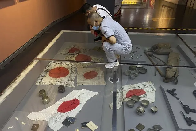 Visitors wearing masks look at captured Japanese flags at The Museum of the War of Chinese People's Resistance against Japan in Beijing, Tuesday, September 27, 2022. Friend or foe? Or both? On the streets of Tokyo and Beijing, the ties between Japan and China remain complicated and often contradictory, 50 years after the two countries normalized relations as part of a process that brought communist China into the international fold. (Photo by Ng Han Guan/AP Photo)