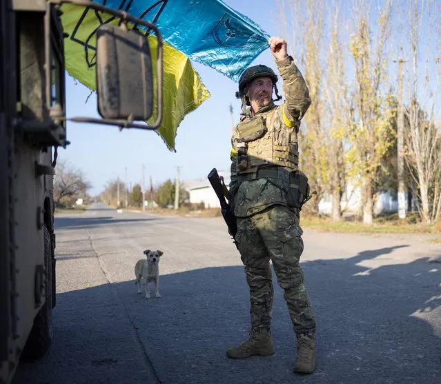 A soldier holds a weathered Ukrainian flag as the sun begins to set on the freshly recaptured town in Snihurivka, Ukrainian southern Mykolayiv region on November 10, 2022. (Photo by Andriy Dubchak/Radio Free Europe/Radio Liberty)