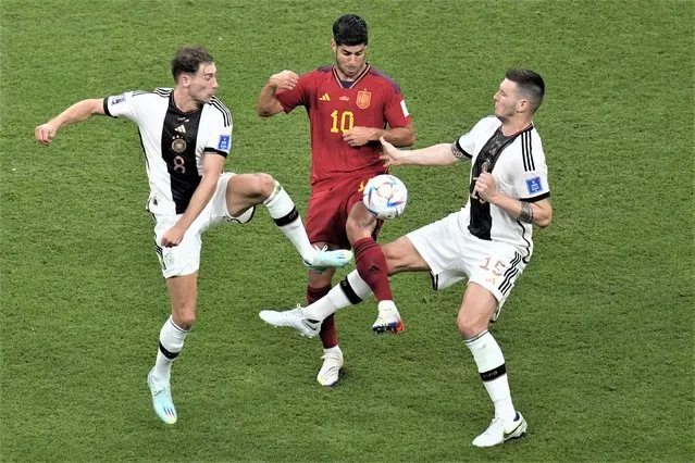 Spain's Marcos Asensio, centre, challenges for the ball with Germany's Leon Gorentzka, left, and Germany's Niklas Suele during the World Cup group E soccer match between Spain and Germany, at the Al Bayt Stadium in Al Khor, Qatar, Sunday, November 27, 2022. (Photo by Ricardo Mazalan/AP Photo)