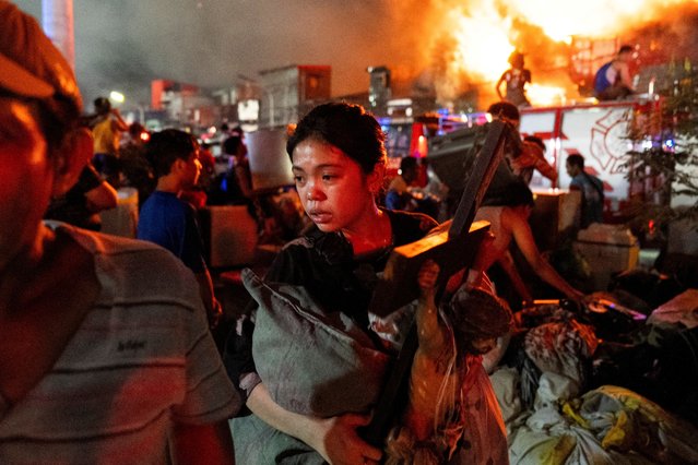 A woman carries a crucifix as she escapes the fire at a residential area in Manila, Philippines, on April 23, 2025. (Photo by Lisa Marie David/Reuters)