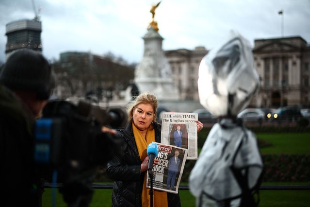 A broadcast journalist shows newspaper frontpages on Britain's King Charles III's cancer while reporting from outside Buckingham Palace in London on February 6, 2024. King Charles III has been diagnosed with cancer and has begun treatment, Buckingham Palace said on February 5, sparking a flood of support from around the world. (Photo by Henry Nicholls/AFP Photo)