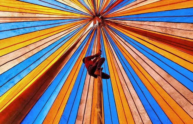 A circus worker climbs into what appears to be a colourful abyss. The worker was actually climbing up a tent pole as they prepared the stage at the 512 year old Gupinathpur fair in Joypurhat, Bangladesh on January 9, 2023. Estiak Ahmed Munna, 29, said: “It is a dangerous job, the pole is about 25 feet tall, but the workers are very experienced. They go to the top of the pole to decorate the circus stage. The workers are usually in the profession since their childhood and have seven to ten years experience. There are more than one hundred circus groups in Bangladesh, with about 20,000 people employed in the profession”. (Photo by Estiak Ahmed Munna/Solent News & Photo Agency)