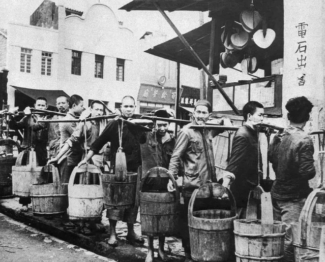 Chungking's water is a commodity on sale at certain distribution centers. Here, a line of coolies wait to fill their wooden tubs, carried in old-time milkmaid fashion, slung from a shoulder strut in China, July 29, 1944. (Photo by AP Photo)