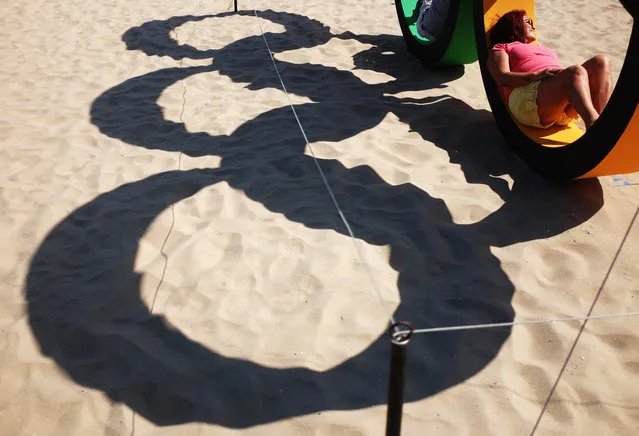 The Olympic rings cast a shadow on the sand as visitors pose for photos along Copacabana Beach ahead of the upcoming 2016 Summer Olympics in Rio de Janeiro, Brazil, Tuesday, August 2, 2016. The iconic Copacabana beach will be the starting point for the road cycling race, marathon swimming and triathlon competitions during the Olympics. (Photo by David Goldman/AP Photo)