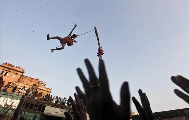 A Hindu devotee hanging from a rope throws offering towards other devotees during the “Chadak” ritual in Kolkata April 14, 2013. Hundreds of Hindu devotees attend the ritual, held to worship the Hindu deity of destruction Lord Shiva, on the last day of the Bengali calendar year. (Photo by Rupak De Chowdhuri/Reuters)