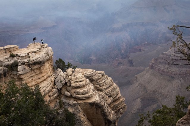 A couple takes pictures from an outcropping as smoke from the Dragon Bravo fire fills the Grand Canyon on July 17, 2025 in Grand Canyon, Arizona. Despite recent rains, two wildfires have been burning out of control near the North Rim of the canyon, fueled by recent strong winds, high temperatures and low humidity. (Photo by Scott Olson/Getty Images)