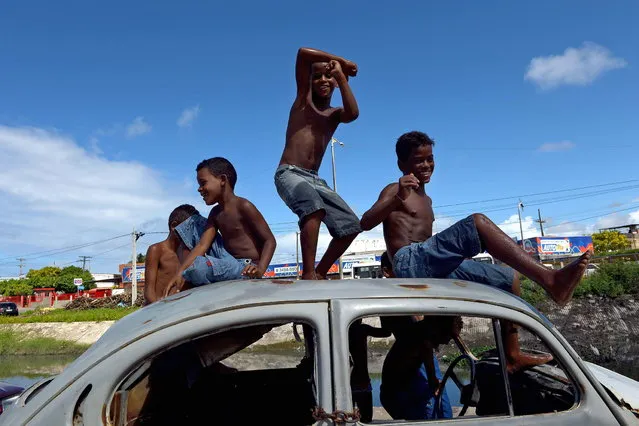 Boys look at friends playing football from an abandoned Volkswagen Beetle in a shantytown of Olinda, about 18 km from Recife in northeastern Brazil, on June 18, 2013 as the FIFA Confederations Cup Brazil 2013 football tournament is being held in the country. The historic centre of Olinda is listed as an UNESCO World Heritage Site. (Photo by Vincenzo Pinto/AFP Photo)