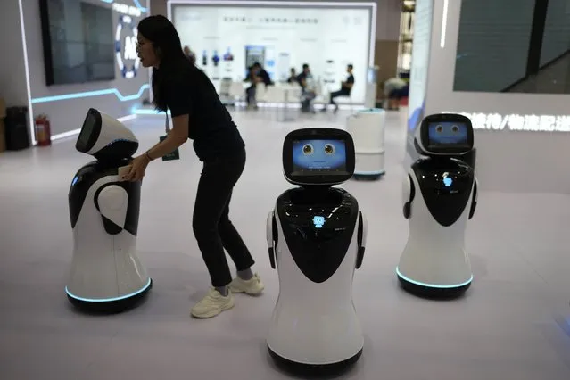 A woman pushes robots around at the annual World Robot Conference at the Beijing Etrong International Exhibition and Convention Center, Wednesday, August 16, 2023. (Photo by Ng Han Guan/AP Photo)