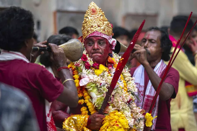 Local musicians blow horns as a Hindu priest, face smeared with color and sacrificial blood, performs rituals during the Deodhani festival at the Kamakhya Hindu temple in Guwahati, India, Saturday, August 19, 2023. Goats and pigeons are commonly offered as sacrifice in the belief that participants receive supernatural power from goddess Kamakhya during the festival held to worship the serpent Goddess. (Photo by Anupam Nath/AP Photo)