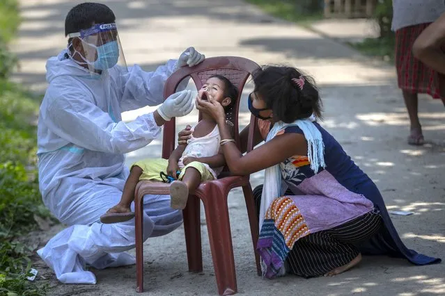 An Indian health worker in protective suit takes the swab of a child to test for COVID-19 in Burha Mayong village, Morigaon district of Assam, India, Saturday, May 22, 2021. (Photo by Anupam Nath/AP Photo)