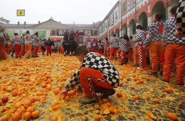 A boy collects oranges during the traditional orange-throwing battle in the northern Italian Piedmont town of Ivrea, Italy, Tuesday, February 9, 2016. The Carnival orange-throwing battle has its roots in the middle of the 19th century. (Photo by Luca Bruno/AP Photo)