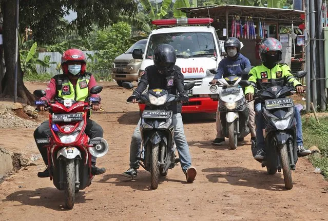 Motorcycle volunteers escort an ambulance carrying the body of a COVID-19 victim on its way to a cemetery for burial, in Bekasi on the outskirts of Jakarta, Indonesia on July 11, 2021. The two-wheeled volunteers provide a key service in the sprawling metropolis, one in more need than ever as ambulances struggle to serve all those in need because of a surge in coronavirus infections and deaths. (Photo by Achmad Ibrahim/AP Photo)