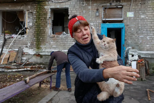 Local resident Rita holds a cat while her neighbour Raisa saws firewood next to their residential building heavily damaged by permanent Russian military strikes in the front line town of Avdiivka, amid Russia's attack on Ukraine, in Donetsk region, Ukraine on November 8, 2023. (Photo by Serhii Nuzhnenko/Radio Free Europe/Radio Liberty via Reuters)